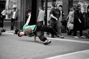 A young man break-dances in the street. He uses a difficult move of balancing his entire body on the strength of one hand.
